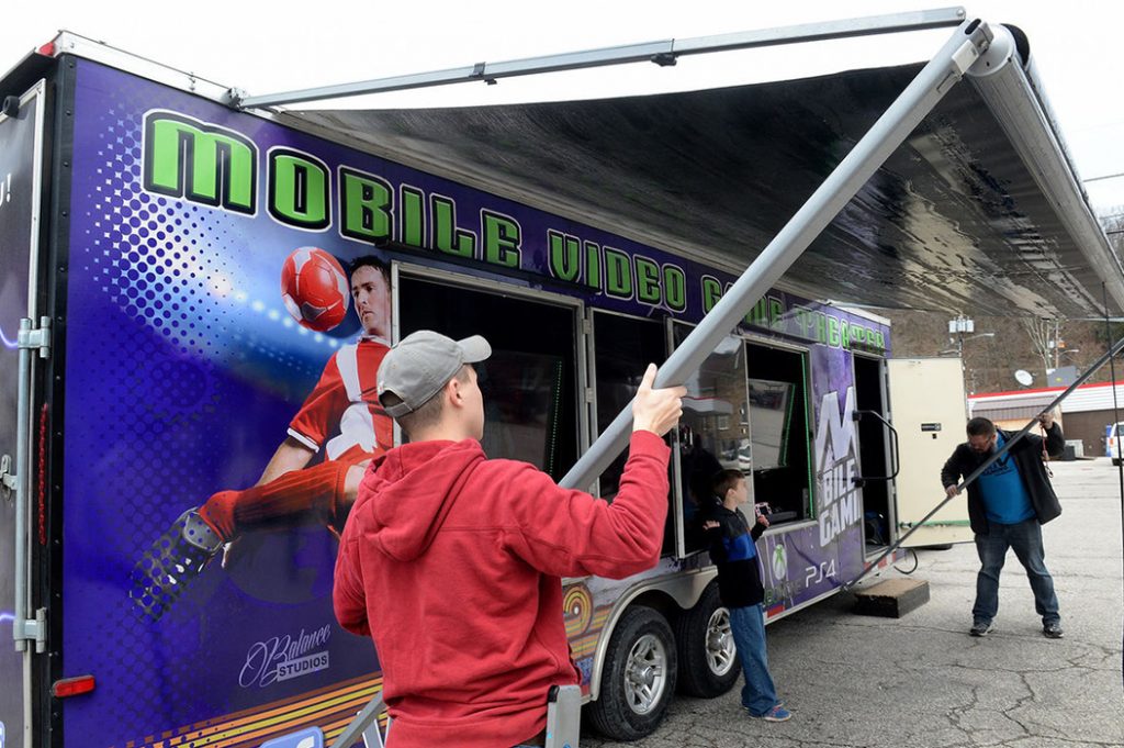 Justin Paxton helps Craig Petry set up his mobile video gaming trailer Monday in a Clendenin parking lot. Petry, in association with the Kanawha County Library system, is setting up his trailer at library branches for children off from school on Spring Break. Chris Dorst, Gazette-Mail